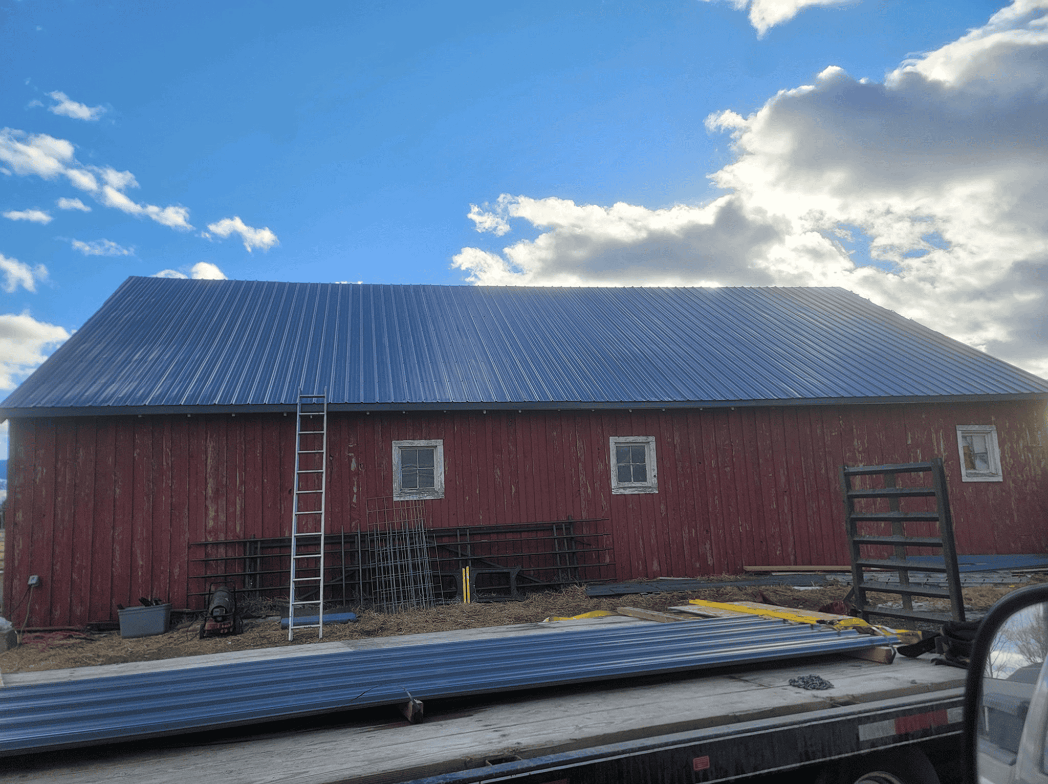 Red barn with new metal roof under a bright blue sky with clouds.