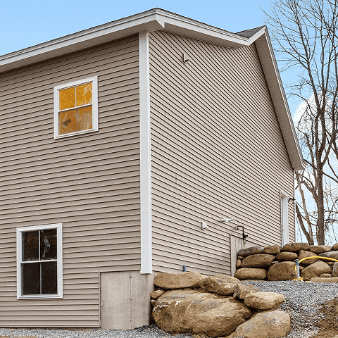 New beige vinyl siding on a residential house with white trim and windows.