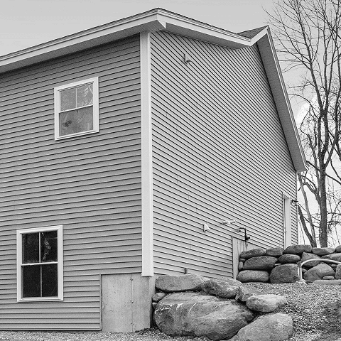New beige vinyl siding on a residential house with white trim and windows.