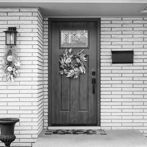 Stylish front door with floral wreath and modern hardware in a brick home.