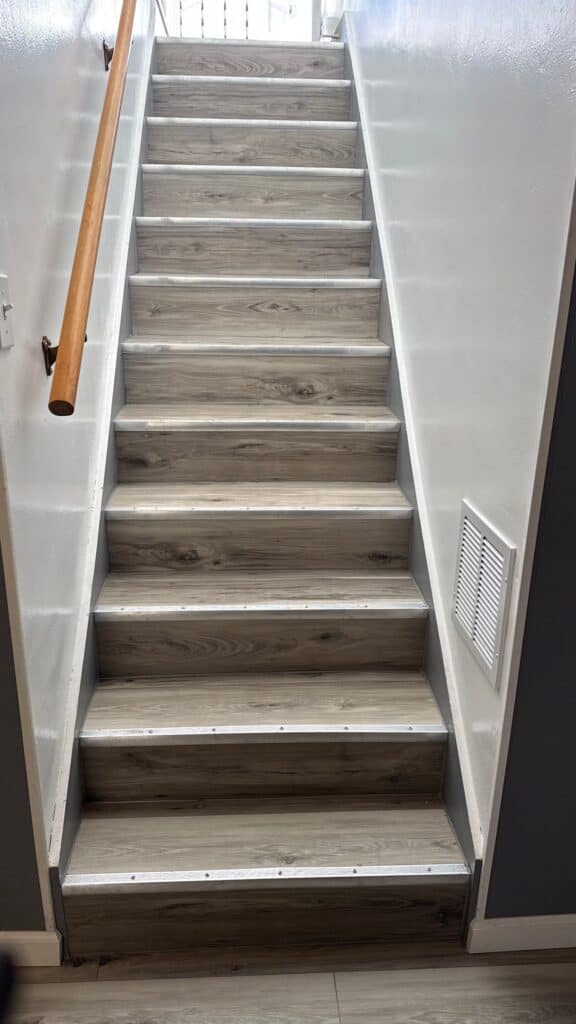 Staircase with Wooden Steps Indoor staircase with wood-look steps and white walls, featuring a wooden handrail on the left side.