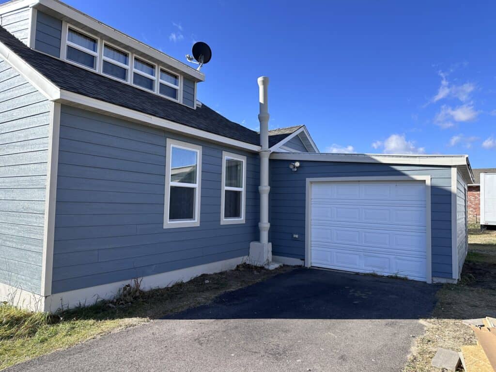 Blue house with white trim and attached garage under a clear blue sky.