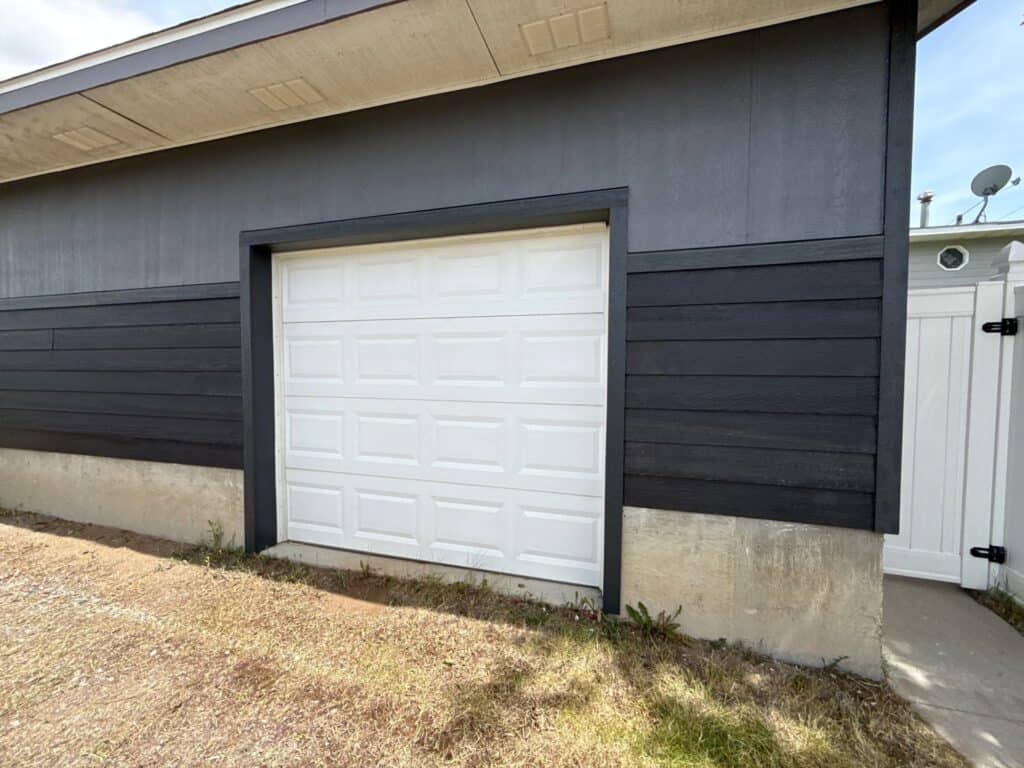 Garage door with white panel design and black siding exterior.