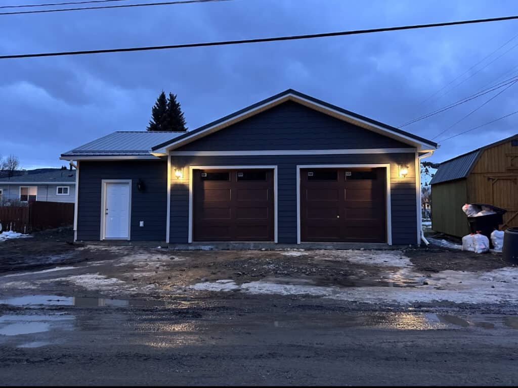 Garage Building with Blue Siding and Double Doors Garage with blue siding, two brown doors, and exterior lighting at dusk.