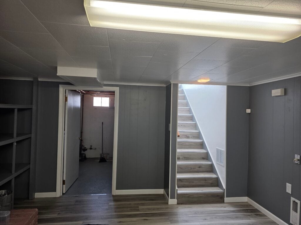 Home Basement Interior Basement interior with stairs and lighting, featuring gray walls and wooden flooring.