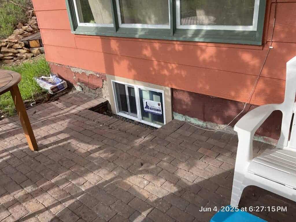 Home Exterior Renovation Basement window installation with brick pavers outside a house with red siding.