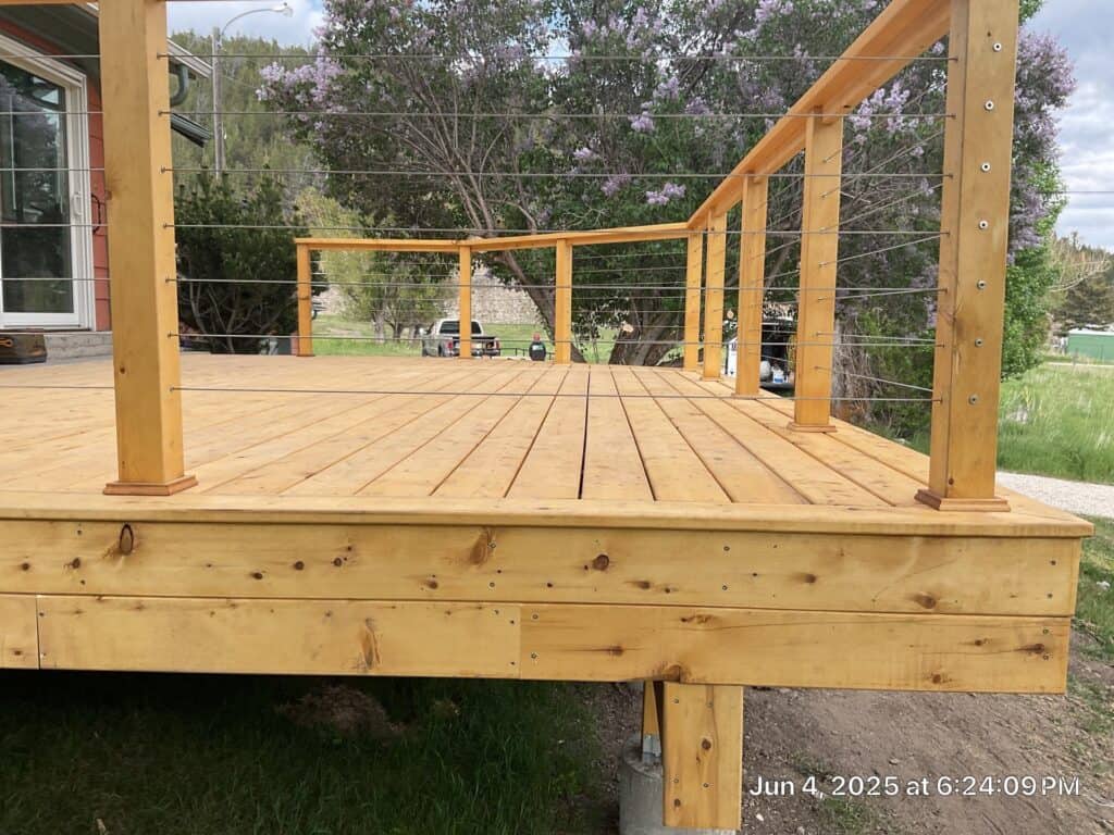 Deck Construction Deck with wooden planks and cable railing in a residential backyard.