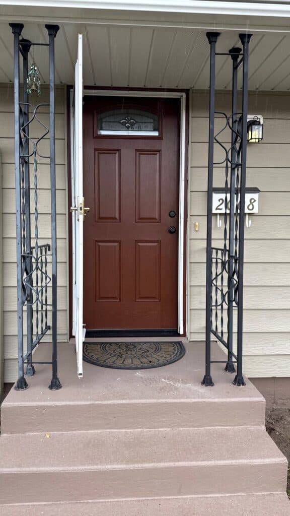 Front Door Entrance Sturdy brown front door with security screen and porch steps.
