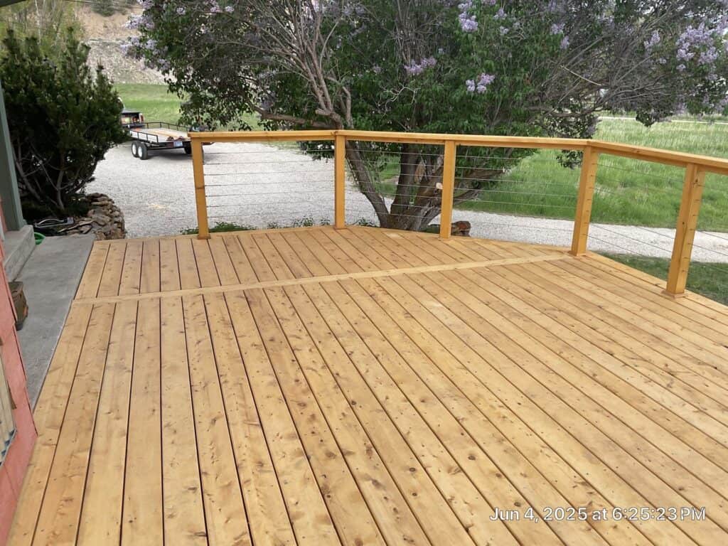 Wooden deck extension New wooden deck extension with railing in a backyard setting.