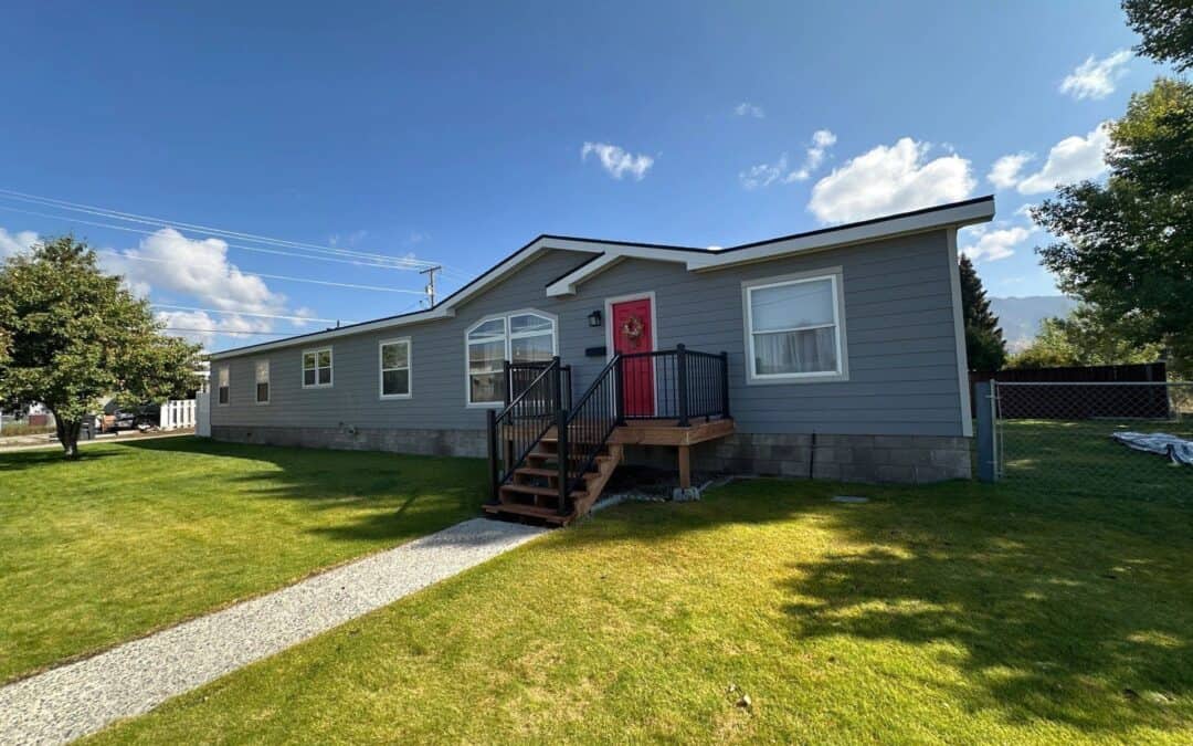 Modern manufactured home with blue siding and a red front door in a sunny yard.