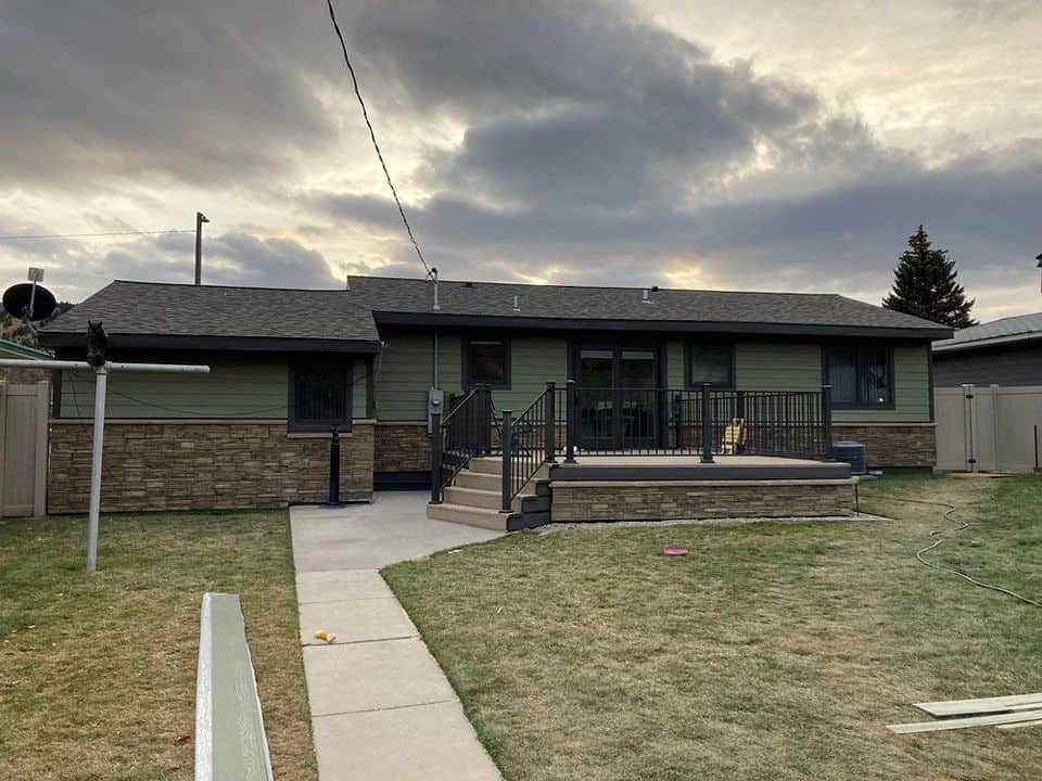 Modern house with a green and brick facade, front porch, and well-maintained lawn.