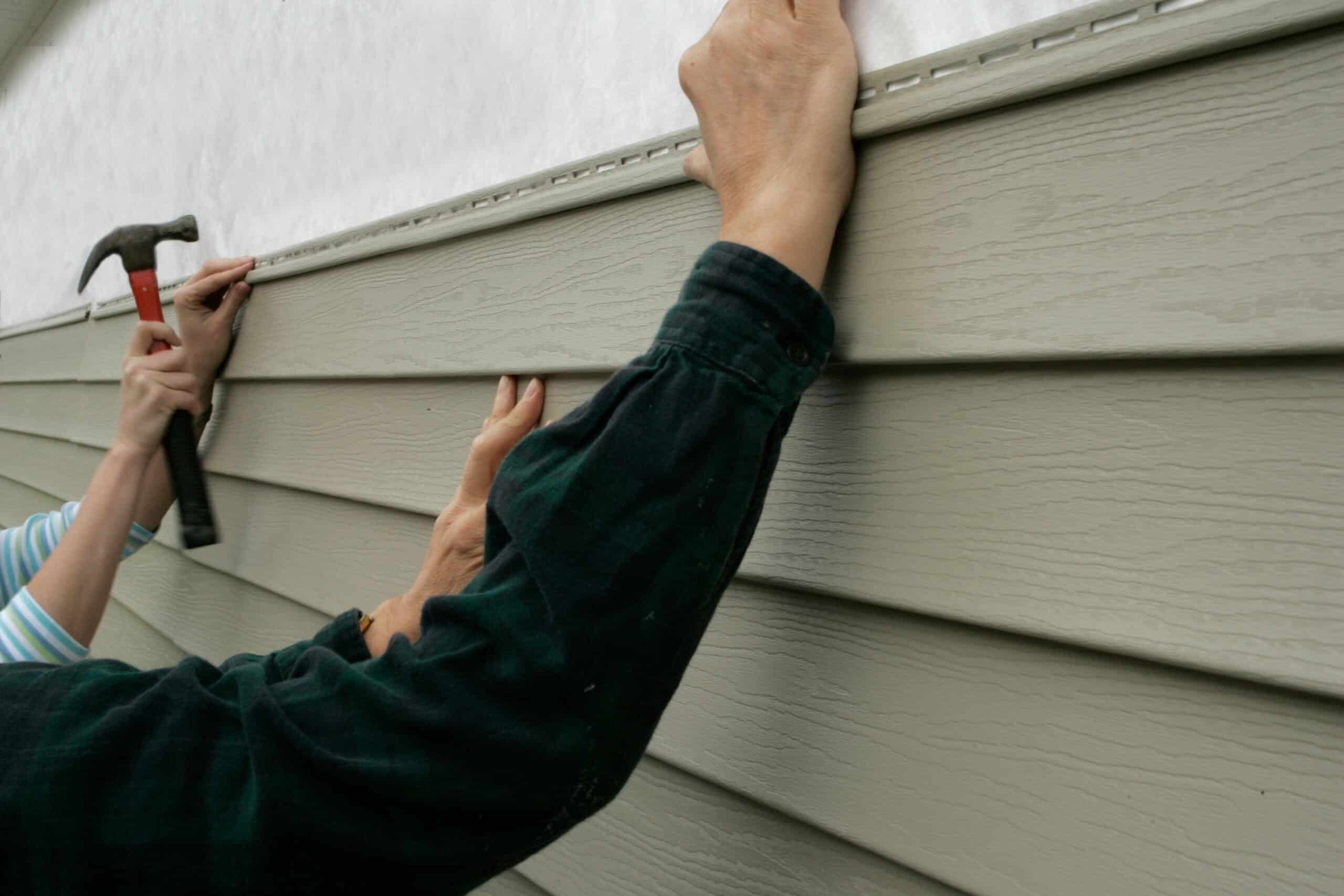 Workers installing vinyl siding on a house exterior with tools.