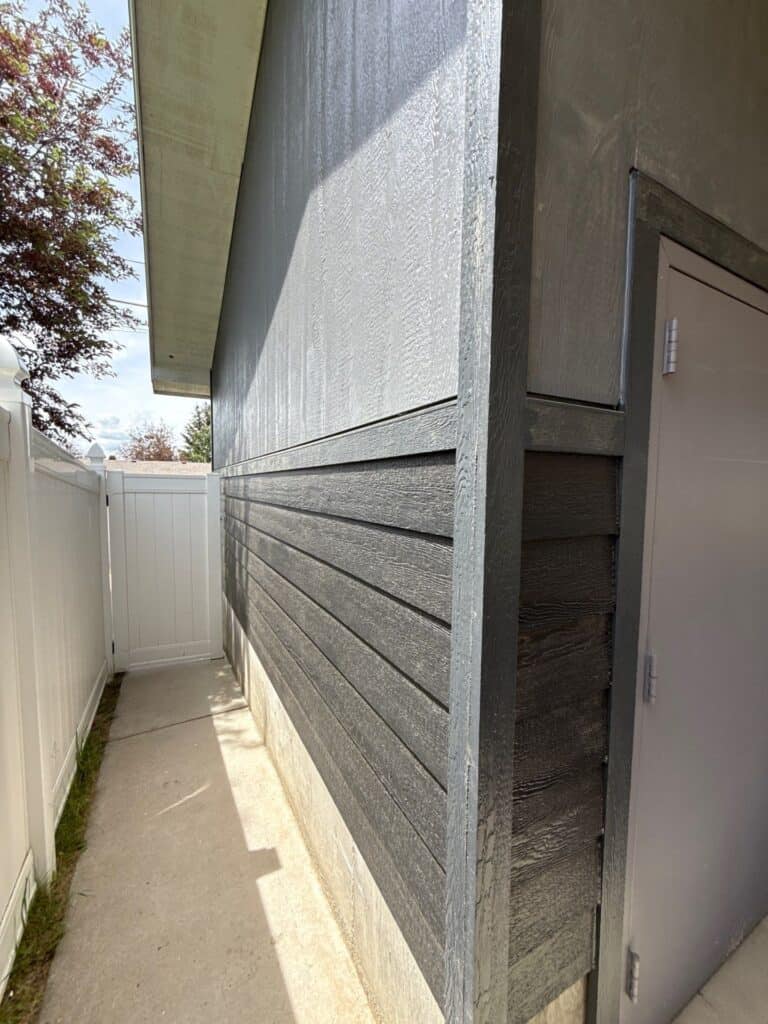 Close-up of modern house siding with textured gray panels and a side door.
