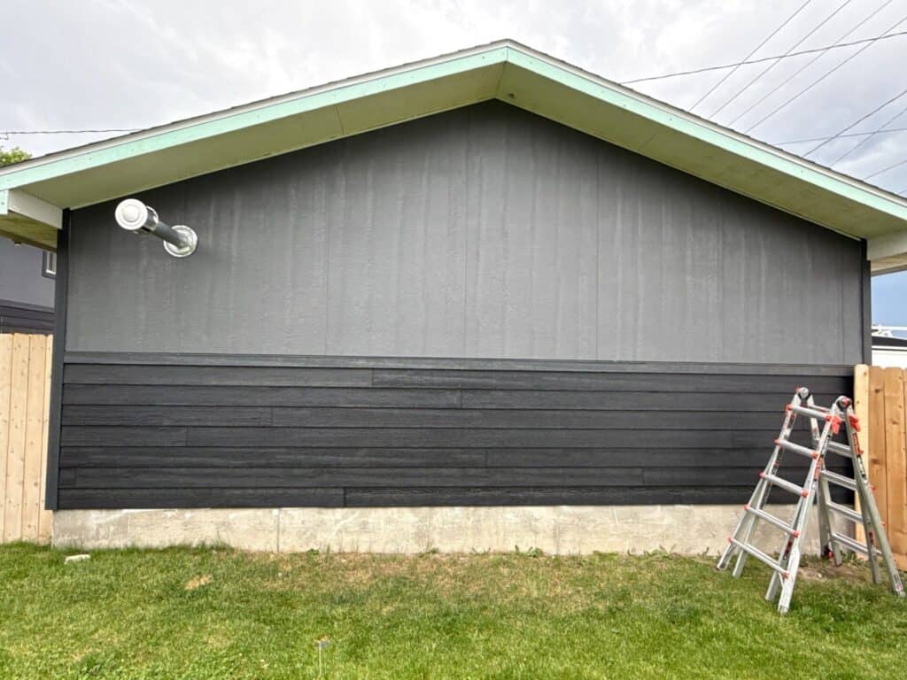 House exterior painted in dark gray with light green trim, ladder nearby, under cloudy sky.