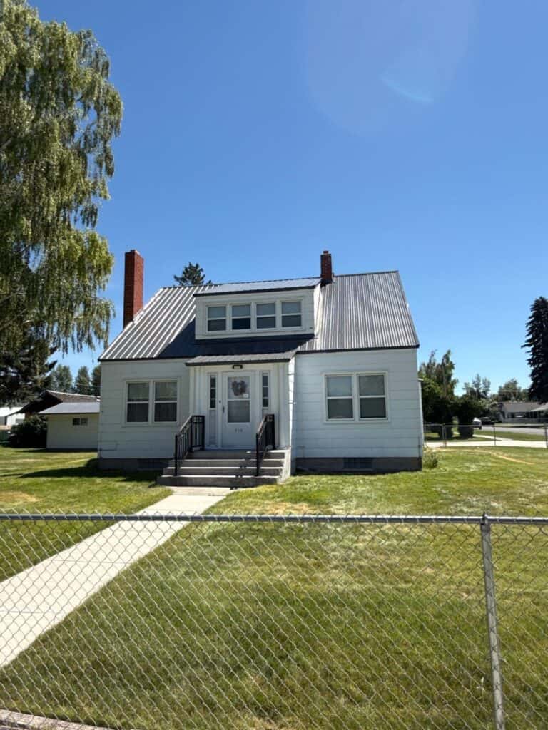 White two-story house with metal roof and front porch under clear blue sky.