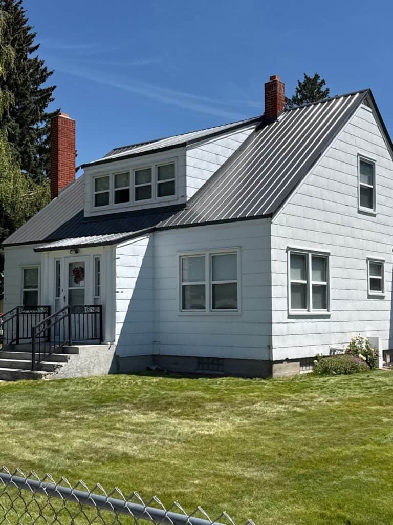 White house with metal roof and multiple windows in a lush green yard.