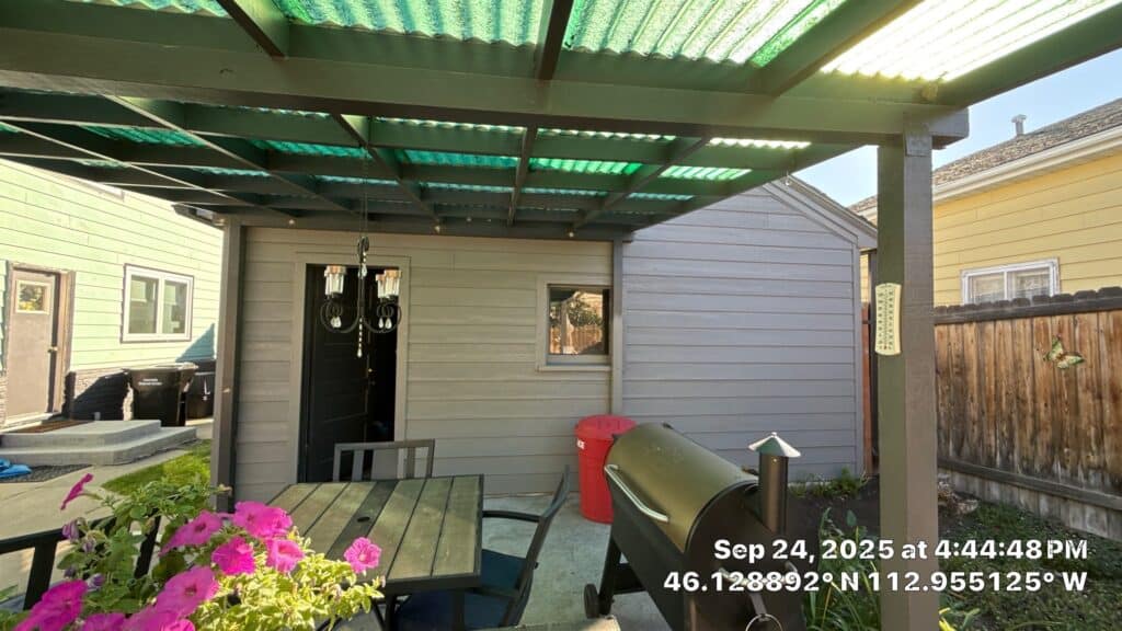 Covered outdoor patio with dining table, grill, and garden view in a residential backyard.