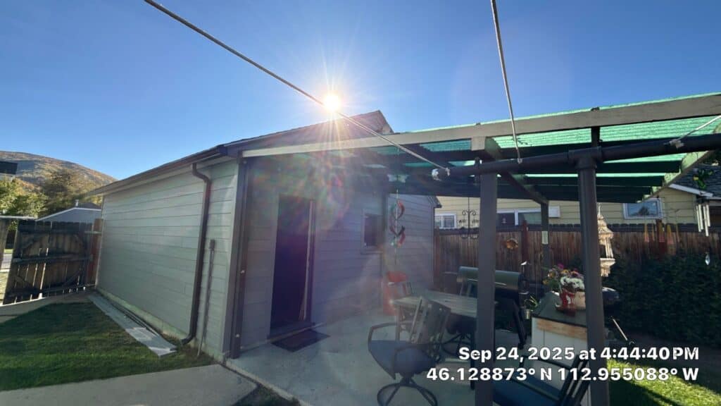 Backyard building with green roof and wooden fence under clear blue sky.