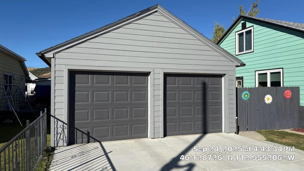 Modern double garage with black doors and concrete driveway in residential area.