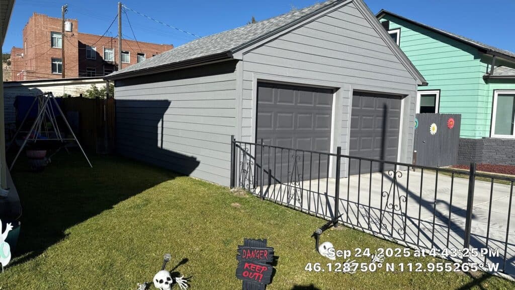 Gray garage with two doors and a metal railing in front, residential neighborhood.