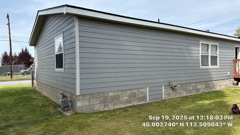 Exterior view of a gray residential house with a concrete foundation and white window frames.