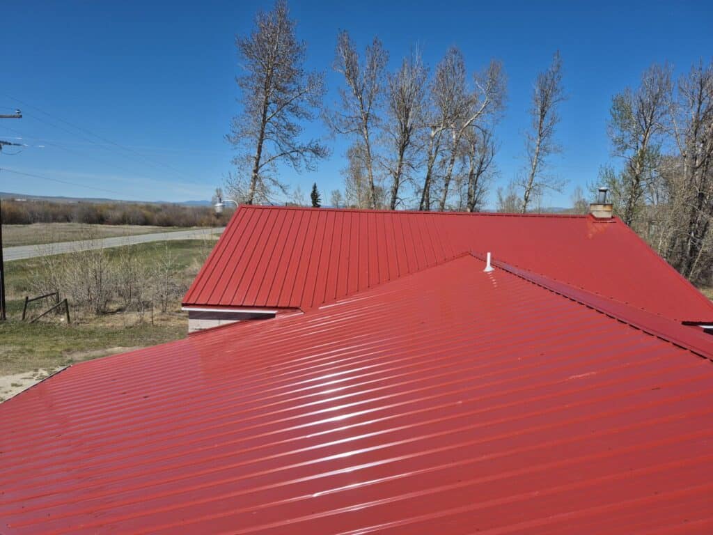 Red metal roof on a rural building with trees and blue sky in background.