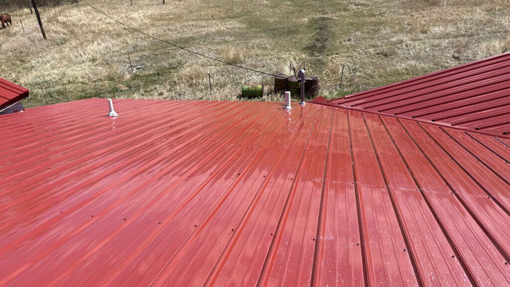 Red metal roof with a curved design on a building in an open field.