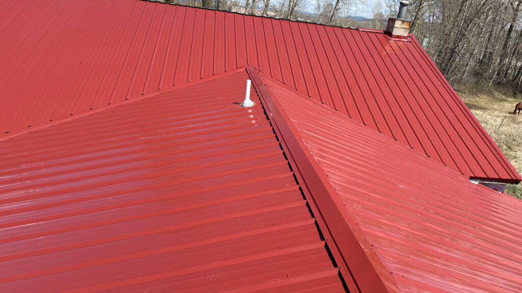Close-up of a red metal roof with standing seam panels and a chimney pipe.