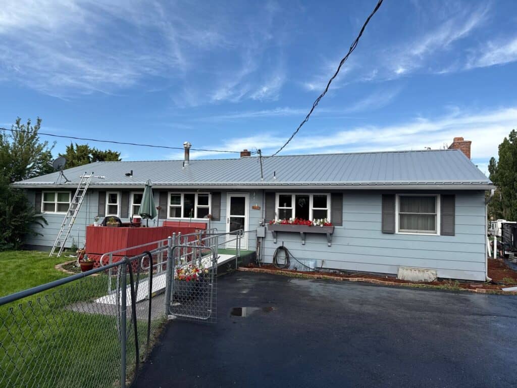 Single-story house with light blue siding, metal roof, and front yard garden.