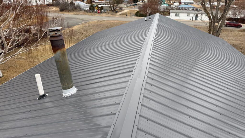 Close-up of a metal roof with vents and chimney in a residential area.