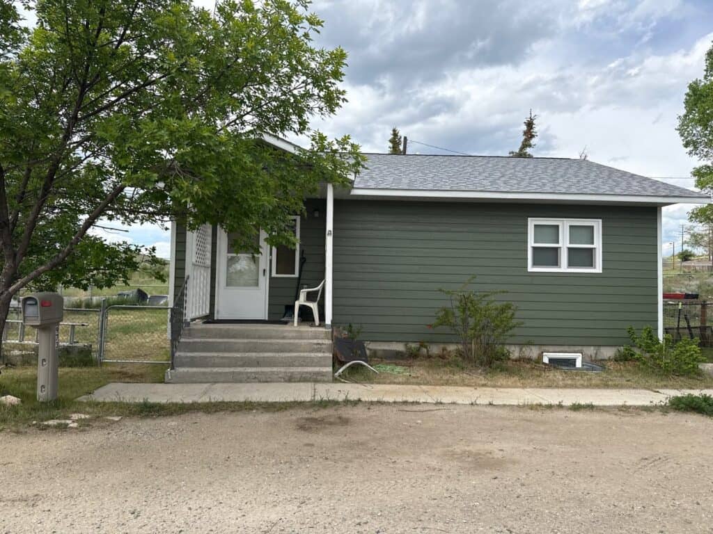 Small green house with white trim and front steps in a residential neighborhood.