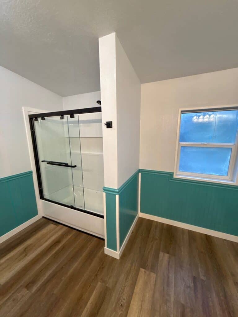 Modern bathroom with glass shower enclosure and teal wall paneling.