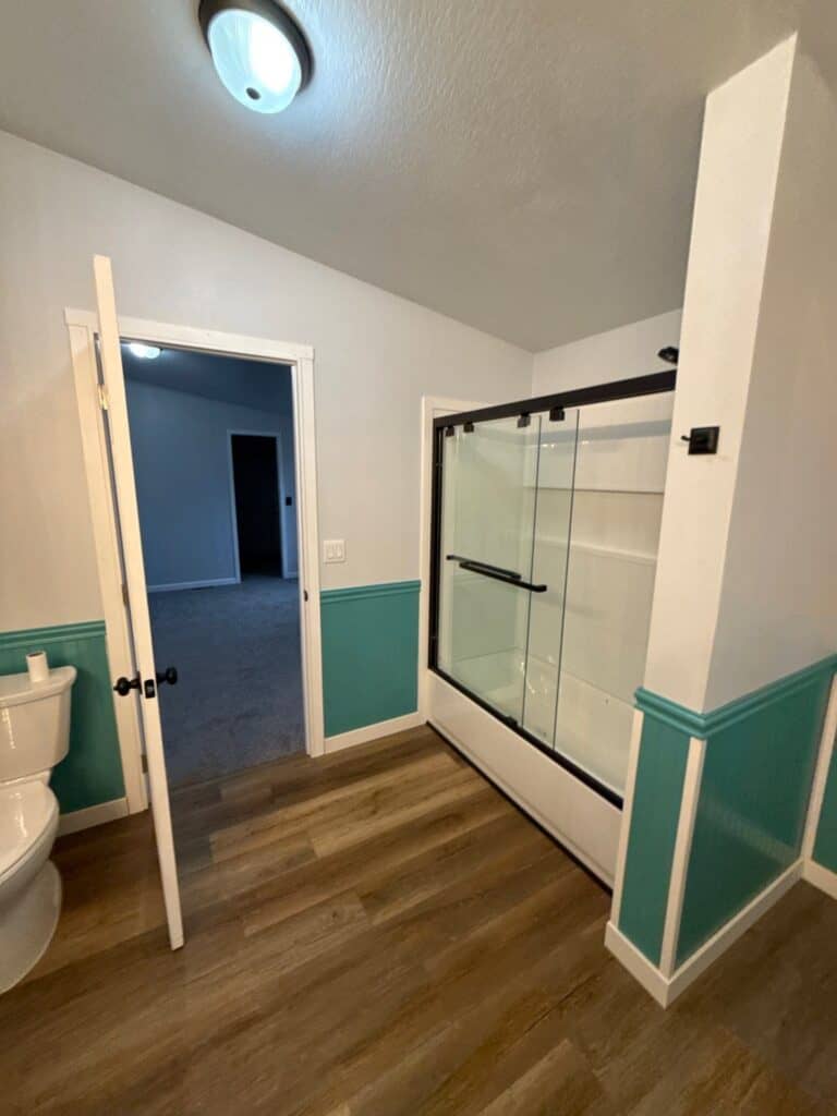Modern bathroom with glass shower enclosure and teal wall accents.