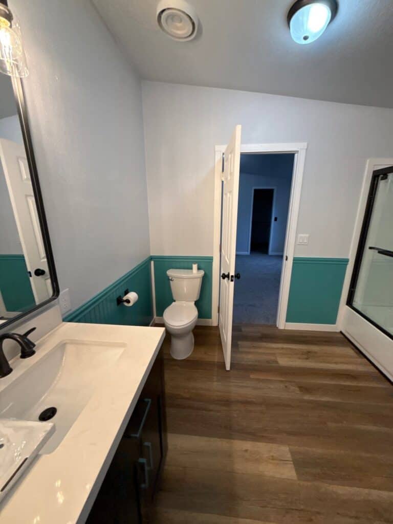 Modern bathroom with white walls, teal wainscoting, and wooden flooring.