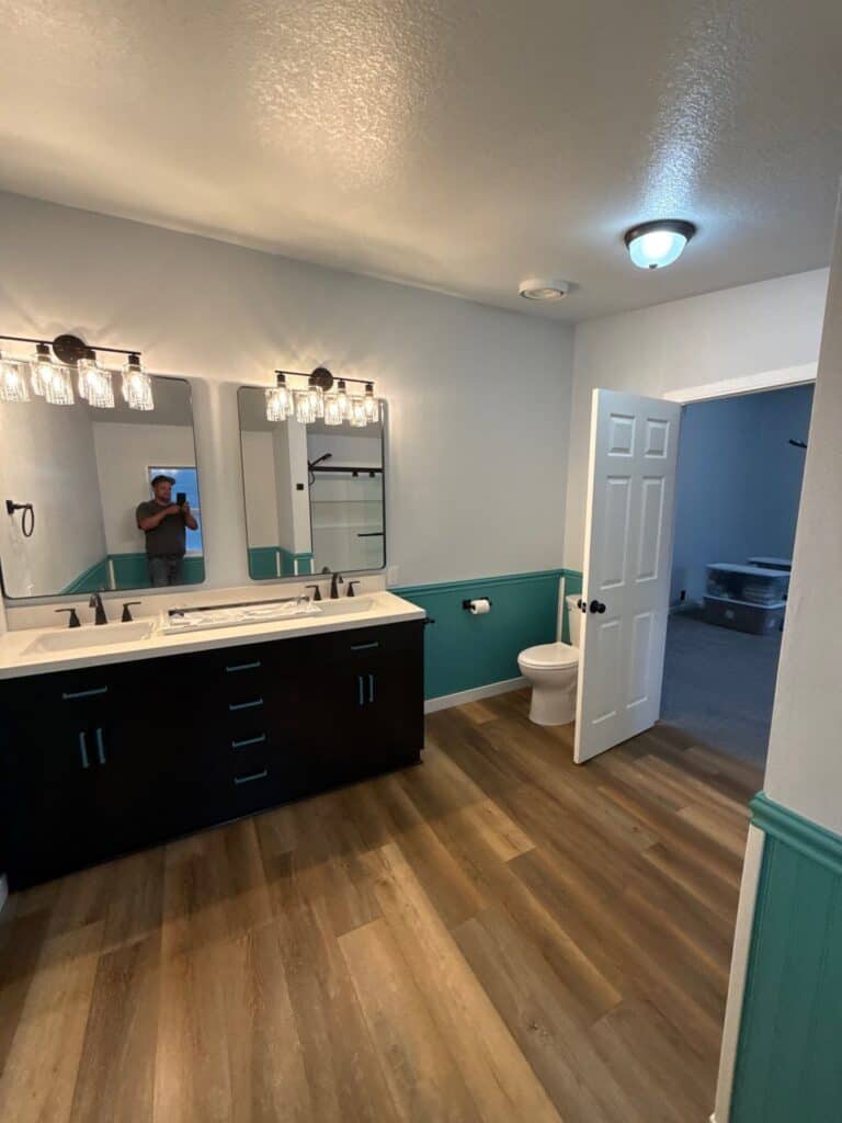 Modern bathroom with dual sinks, large mirror, and wood flooring.