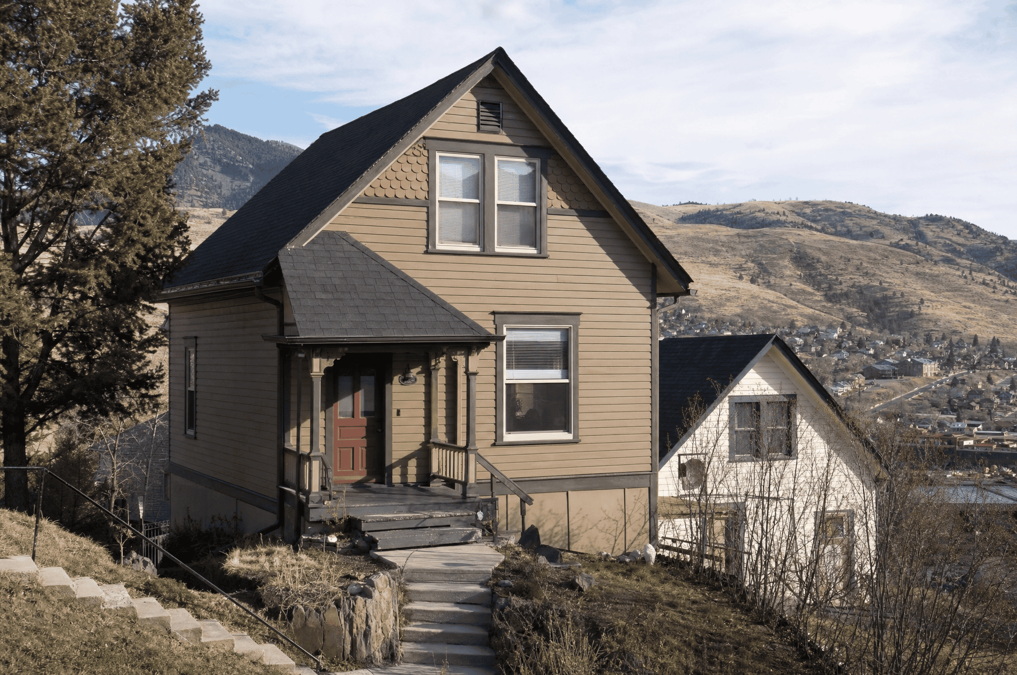 Charming mountain house with beige siding and black roof, scenic background with hills and sky.